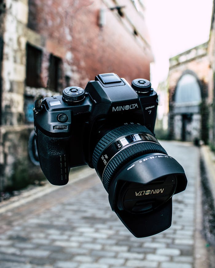 Close-up of a Minolta camera floating in an urban alley, showcasing optical technology.